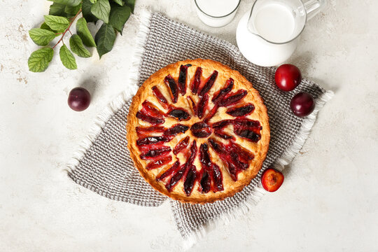 Tasty plum pie and jug of milk on light background