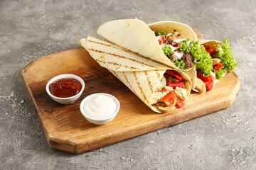 Wooden board with tasty Fajitas and sauce on grunge background