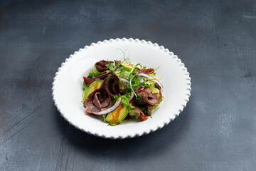 Salad with meat and avocado in a plate. On a gray background.