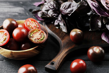 Fresh ripe black cherry tomatoes with basil on textured background