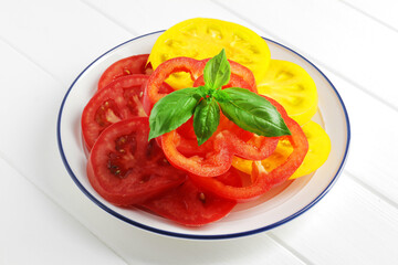 Plate full of slices of fresh tomatoes of different varieties on wooden background