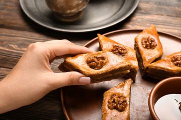 Woman taking tasty baklava from plate on wooden background, closeup
