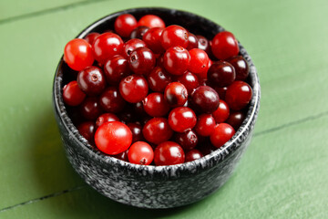 Bowl with healthy cranberries on color wooden background