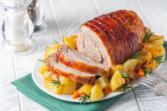 Sliced veal roulade with baked potato and rosemary on white wooden table. Selective focus.
