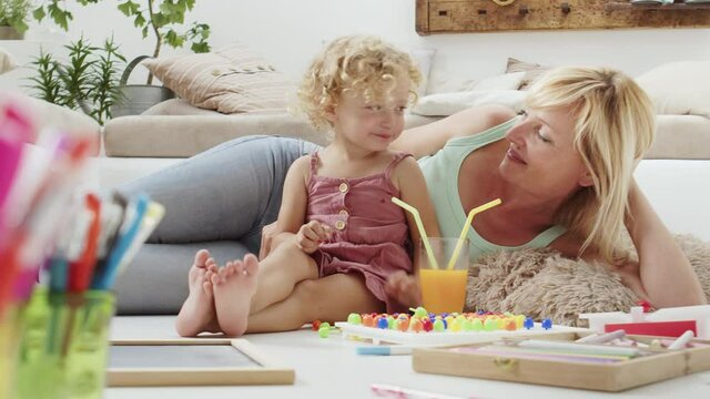 smiling mother smiles at curly haired blonde daughter child, drinking cheerfully from the same glass dividing orange juice with straws, preschool learning activity at home, concept of healthy growing