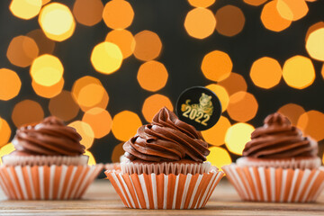 Tasty cupcakes for New Year 2022 celebration on table against blurred lights