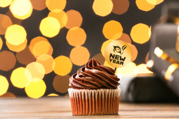 Tasty cupcake for New Year 2022 celebration on table against blurred lights