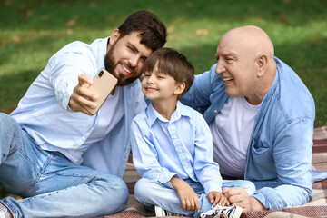 Happy man, his little son and father taking selfie in park