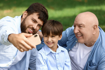 Happy man, his little son and father taking selfie in park