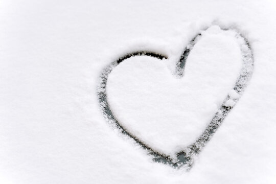 Close up view of the heart shape drawn on a car windshield covered with fresh white snow. Winter concept. Stock photo