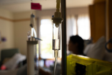 Close up on an IV drip with blurry hospital room in the background.