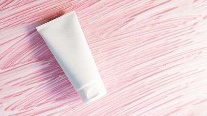 white cosmetic tube on a pink background with soap foam and bubbles. Face or body cleancer concept. Copy space