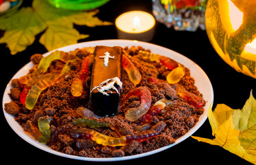 Marmalade worms in ground made of crumbled chocolate cookies and coffin. Halloween food, decor dessert for kids. Chocolate Halloween dessert with gummy worms, selective focus.