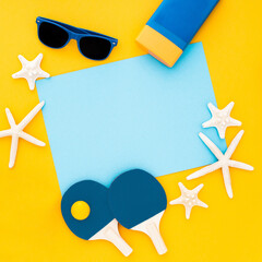 Summer yellow-theme composition with sunglasses, ping pong paddles, starfish and blue copy space