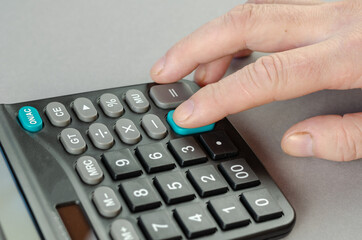 The man's index finger presses the green plus key of the calculator. The businessman performs...