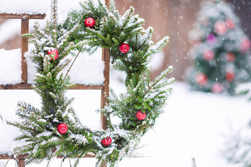 Fototapeta na wymiar Snowy fir tree branches woven into wreath and decorated with red Paradise apples, decoration hanging in the yard in Christmas tree background. Christmas, winter, New year holiday concept 