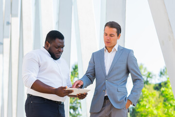 African-American businessman and his colleague in front of modern office building. Financial investors are talking outdoor. Banking and business concept.