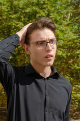 Student with acne on his face is fixing his hair with his hand. Man in a black shirt and glasses. City Park. Outside. Autumn time.