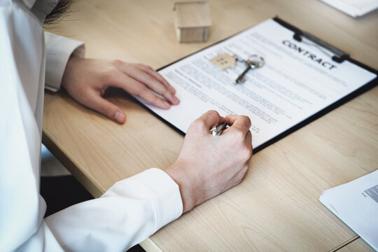 The customer is holding a pen and is reading the housing purchase contract before signing it.