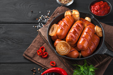 Fried sausages in a frying pan close-up on a black wooden background. Side view, space for copying.