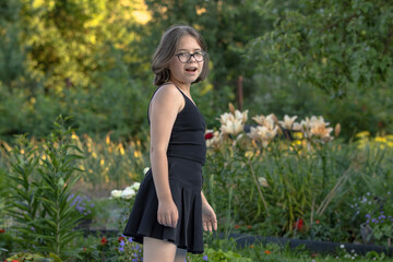 Fototapeta premium Girl in glasses in black clothes is surprised in a blooming summer garden