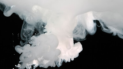 White watercolor ink in water on a black background. Waves of milky ink and splashes of white paints in the water.