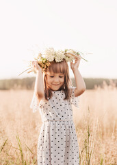 Little pretty girl in a wreath of flowers on her head in nature in the summer