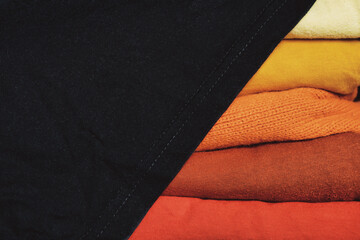 A stack of multi-colored fabric in warm colors. Background with folded clothes in red and yellow tones with empty space for information. T-shirts of different colors