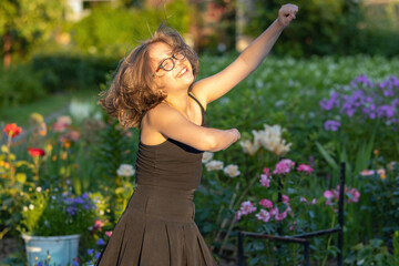 Girl in glasses with long hair dancing in a blooming summer garden