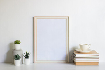 A white blank photo frame with books, coffee and plants over the white background. 