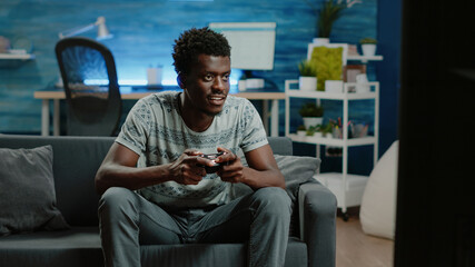 Black man using controller and console to play video games on television for free time activity....