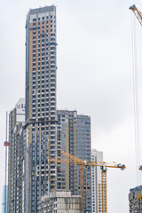 Fototapeta na wymiar Construction cranes and unfinished residential buildings against grey sky. Housing construction, apartment block with scaffolding