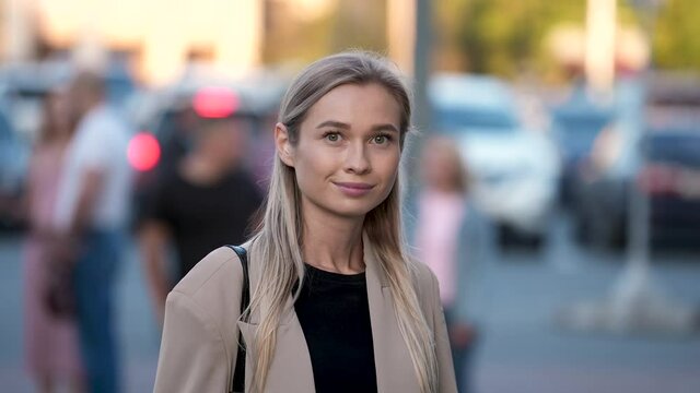 Portrait of looking at camera young adult businesswoman. Casual business lady with trendy look posing. Woman with green eyes and natural colored blonde hair smiling on urban city street background.