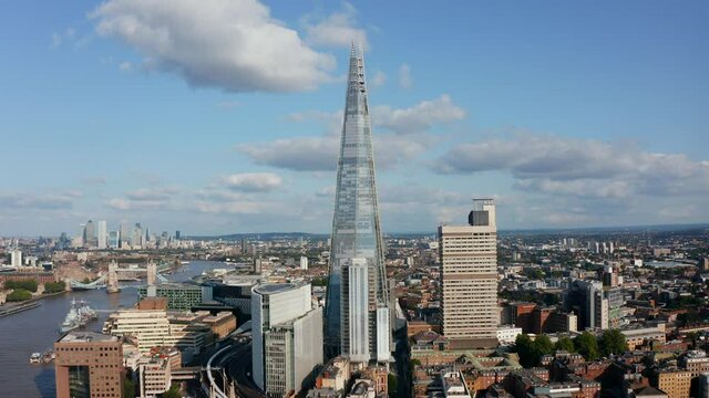 Fly around The Shard skyscraper. Modern futuristic design tall building with conical shape. Historic tower bridge and tall office buildings in Canary Wharf in background. London, UK