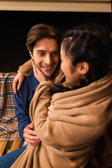Obraz premium Blurred asian woman in blanket touching smiling boyfriend on terrace of glamping house