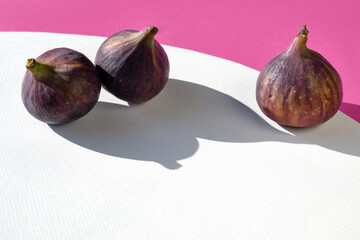 Autumn colors. Purple and magenta fig fruits on vibrant fuchsia and white geometric layered paper. Natural wattle wreath. Sunlight, long shadows.Simple minimal arrangement, copy-space. Brilliant Fall.