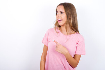 Happy cheerful smiling beautiful blonde girl wearing pink t-shirt on white background looking and pointing aside with hand. Copy space and advertisement concept.