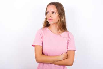 Obraz premium Pleased beautiful blonde girl wearing pink t-shirt on white background keeps hands crossed over chest looks happily aside