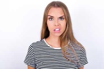 Portrait of dissatisfied beautiful blonde girl wearing striped t-shirt on white background smirks...