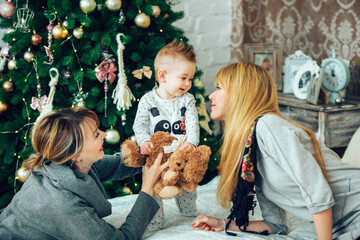 Happy family portrait laying on cosy bed in festively decorated room with Christmas tree. Happy women and one child, all are smiling. Celebrating christmas and new year in lgbt families concept