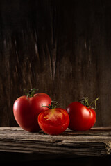 moody portrait of ripe fresh tomatoes with tails on old planks on a wooden background. beautiful artistic dark still life in a rustic style with copy space