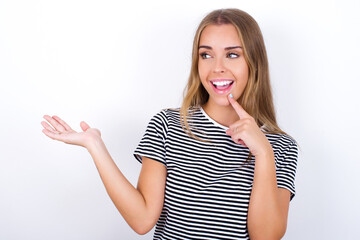 Positive beautiful blonde girl wearing striped t-shirt on white background advert promo touch finger teeth