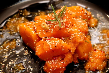 Baked orange pumpkin on a dark plate, decorated with sesame seeds, garlic and rosemary leaves. Autumn pumpkin recipes 