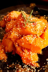 Baked orange pumpkin on a dark plate, decorated with sesame seeds, garlic and rosemary leaves. Autumn pumpkin recipes 