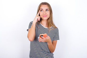 beautiful blonde girl wearing striped t-shirt on white background holding gadget while sticking out tongue