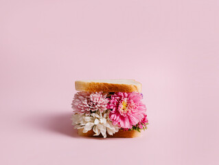 Delicious homemade sandwich with flowers on pastel pink background. Creative floral bloom concept....