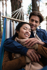 Blurred man embracing asian girlfriend in hammock in autumn