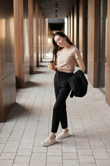 Fototapeta na wymiar Young millennial businesswoman drinking coffee by the office building