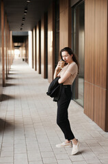 Young millennial businesswoman drinking coffee by the office building