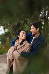 Smiling interracial couple with blanket looking at each other outdoors